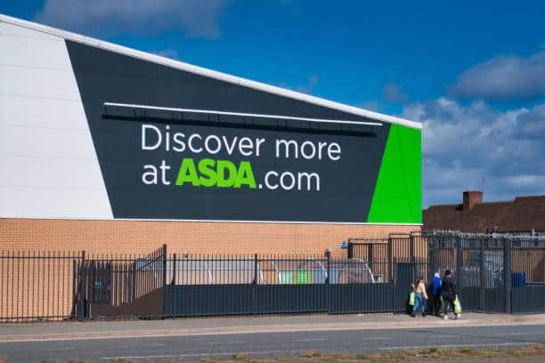Wirral, UK - April 6 2021: Store customers pass corporate signage at a store of the ASDA British supermarket chain, located in a residential area in Wirral the North of England. Taken on a sunny day in spring.